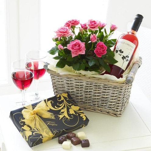 cestino con vino rosato, scatola con cioccolatini e un fascio di rose rosa